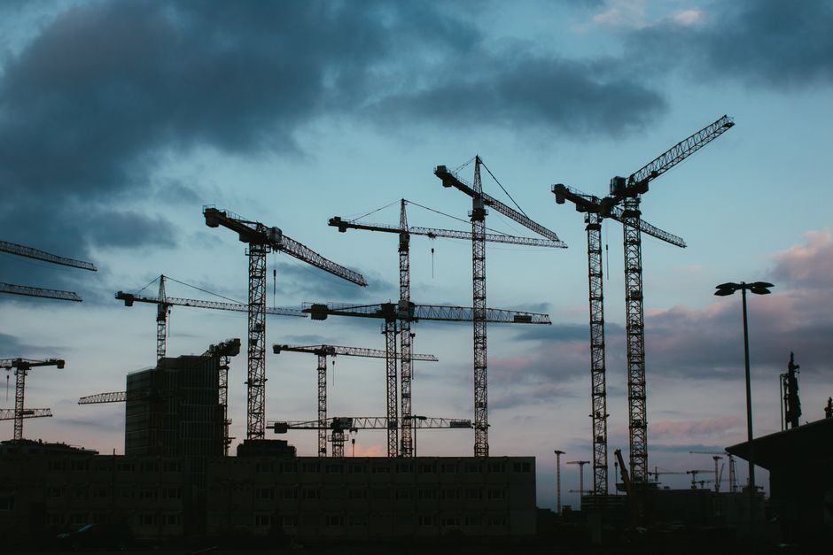 Construction cranes silhouetted against a dusk sky